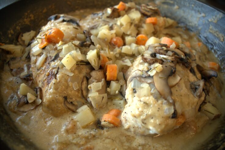 chicken smothered with a potato, carrot, mushroom cream sauce in a cast iron pan.