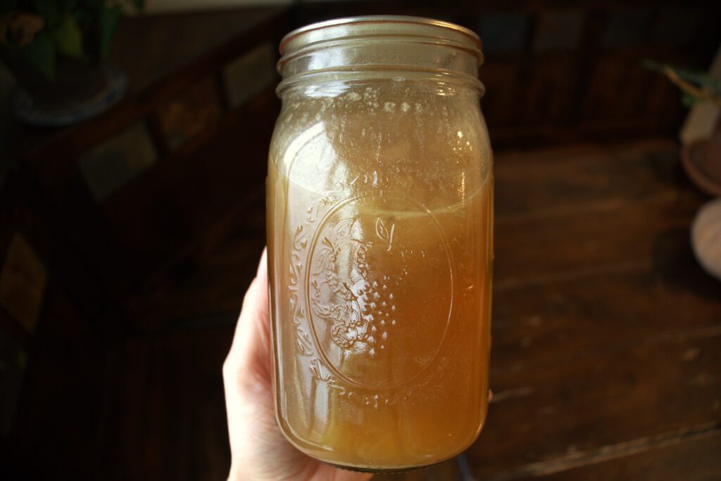Homemade chicken broth sealed in a glass, Ball mason jar with a fruit emblem on the front.