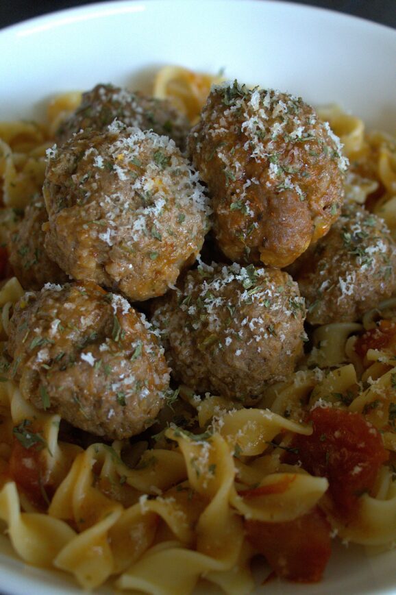Seven meatballs in a bed of egg noodles and red sauce with cheese and cilantro sprinkled over the top