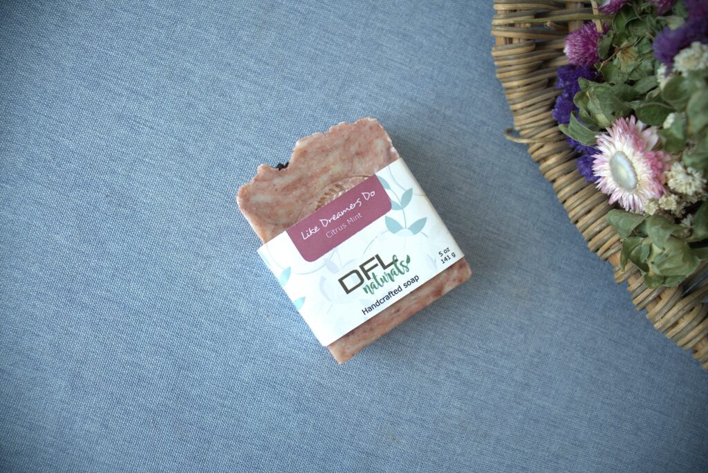 Soap bar next to a basket of flowers on a blue table cloth.