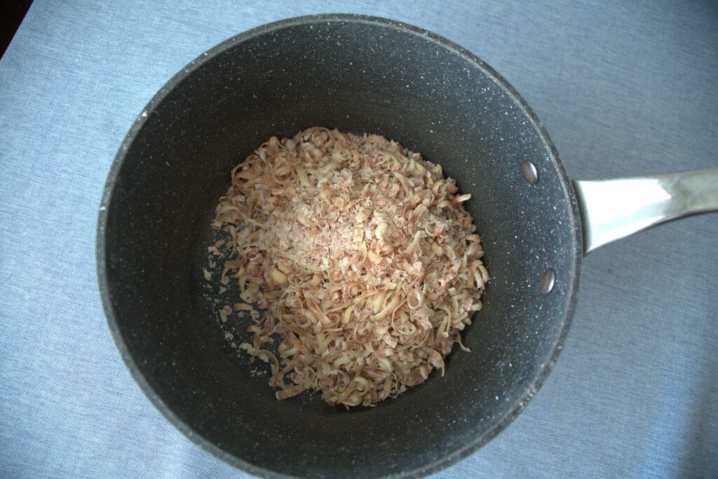 A shredded soap bar in a pot on a blue back drop.